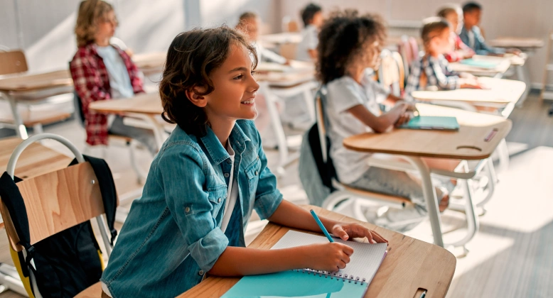 Children sitting in their desks during a lesson. In front is a young boy in a blue shirt.